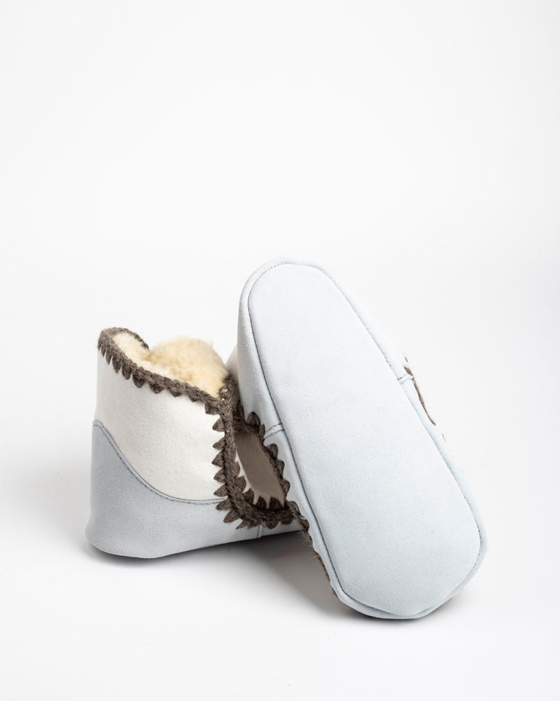 Pair of light gray sheepskin slippers with brown trim on a white background