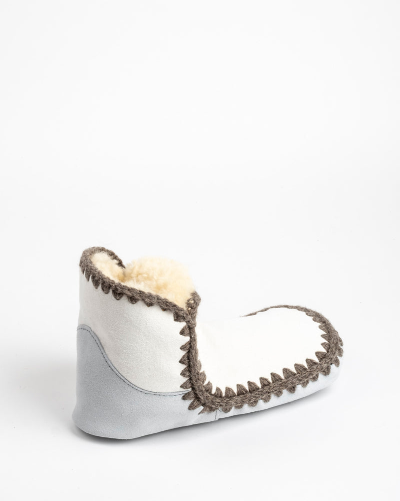 Gray sheepskin slipper with brown trim and white interior on a light gray background
