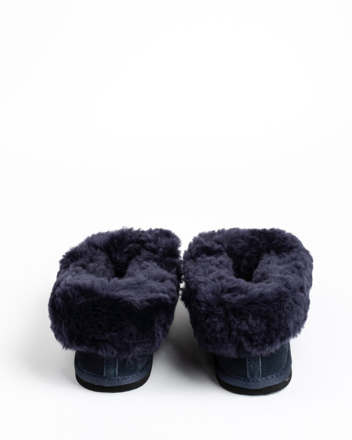 Pair of navy blue sheepskin slippers with fuzzy texture on a white background